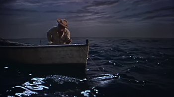 Movie still from “The Old Man and the Sea” (1958), directed by Fred Zinnemann – A man in a straw hat sitting on a boat in the ocean; Wide shot, High angle