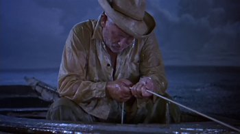 Movie still from “The Old Man and the Sea” (1958), directed by Fred Zinnemann – An old man in a cowboy hat is sitting on the ground and holding a stick; Medium shot, High angle
