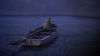 Movie still from “The Old Man and the Sea” (1958), directed by Fred Zinnemann – A man sitting on a boat in the water at night; Wide shot, High angle