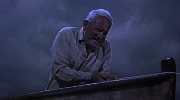 Movie still from “The Old Man and the Sea” (1958), directed by Fred Zinnemann – An older man leaning on a ledge in the dark; Medium shot, Low angle