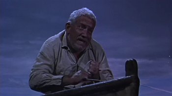 Movie still from “The Old Man and the Sea” (1958), directed by Fred Zinnemann – An older man sitting at a table with a pen in his hand; Medium shot, Low angle