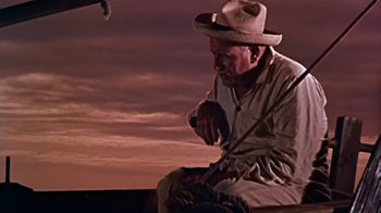 Movie still from “The Old Man and the Sea” (1958), directed by Fred Zinnemann – An old man sitting on a bench in front of a sunset; Medium shot, Low angle