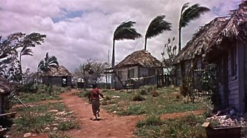 Movie still from “The Old Man and the Sea” (1958), directed by Fred Zinnemann – A man walking down a dirt road in front of houses with palm trees; Extreme Wide shot, Low angle