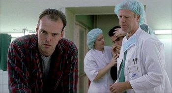 Movie still from “The One and Only” (1999), directed by Susanne Bier – A group of people in a room with a doctor; Medium shot, Low angle