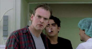 Movie still from “The One and Only” (1999), directed by Susanne Bier – A man standing next to another man smoking a cigarette; Close Up shot, Low angle