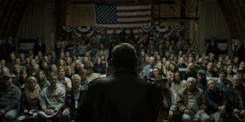 Movie still from “House of Cards” (2013), created by Beau Willimon – A crowd of people sitting in front of an american flag; Wide shot, High angle