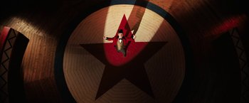 Movie still from “The One and Only Ivan” (2020), directed by Thea Sharrock – A man standing on top of a red and white star; Extreme Wide shot, Overhead angle