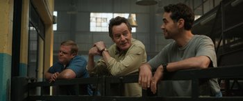 Movie still from “The One and Only Ivan” (2020), directed by Thea Sharrock – A man leaning on a fence with other men; Medium shot, Over the shoulder angle