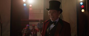 Movie still from “The One and Only Ivan” (2020), directed by Thea Sharrock – An older man wearing a red jacket and a black top hat; Medium shot, Over the shoulder angle