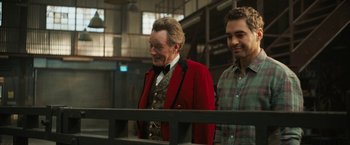 Movie still from “The One and Only Ivan” (2020), directed by Thea Sharrock – A man in a red jacket standing next to another man in a plaid shirt; Medium shot, Over the shoulder angle