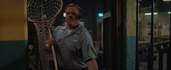 Movie still from “The One and Only Ivan” (2020), directed by Thea Sharrock – A man holding a lacrosse stick while standing next to a door; Medium shot, Low angle