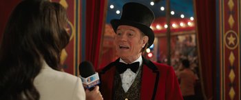 Movie still from “The One and Only Ivan” (2020), directed by Thea Sharrock – A man wearing a top hat talking to a microphone; Close Up shot, Over the shoulder angle