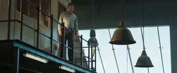 Movie still from “The One and Only Ivan” (2020), directed by Thea Sharrock – A man standing on top of a metal railing next to a window; Wide shot, Low angle