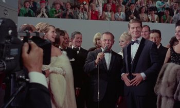 Movie still from “The Oscar” (1966), directed by Russell Rouse – A group of people standing in a room with a microphone; Medium shot, Low angle