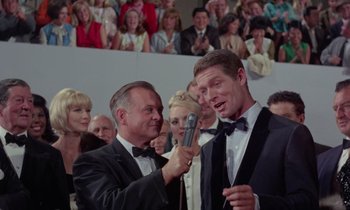Movie still from “The Oscar” (1966), directed by Russell Rouse – Two men in tuxedos are being interviewed by a microphone; Medium shot, Over the shoulder angle