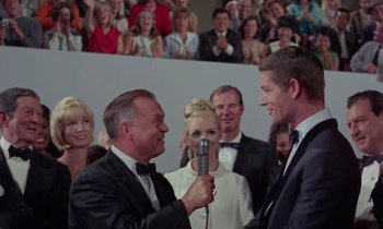 Movie still from “The Oscar” (1966), directed by Russell Rouse – Two men in tuxedos are being interviewed by a microphone; Medium shot, Over the shoulder angle