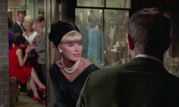 Movie still from “The Oscar” (1966), directed by Russell Rouse – A woman in a black dress talking to a man in a black suit; Medium shot, Over the shoulder angle