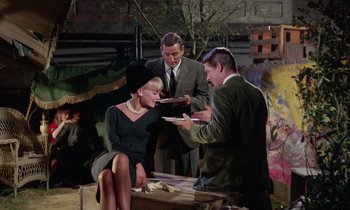 Movie still from “The Oscar” (1966), directed by Russell Rouse – A man and a woman sitting next to each other while another man holds a plate; Medium shot, Over the shoulder angle