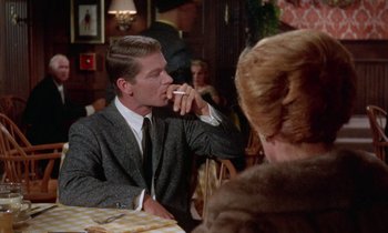 Movie still from “The Oscar” (1966), directed by Russell Rouse – A man sitting at a table with a cigarette in his mouth; Medium shot, Over the shoulder angle