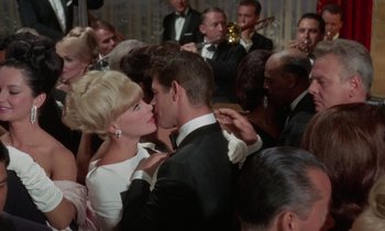 Movie still from “The Oscar” (1966), directed by Russell Rouse – A man and a woman kissing in front of a group of people; Close Up shot, Over the shoulder angle