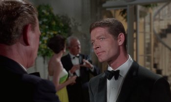 Movie still from “The Oscar” (1966), directed by Russell Rouse – A man in a tuxedo standing in front of other people; Close Up shot, Over the shoulder angle