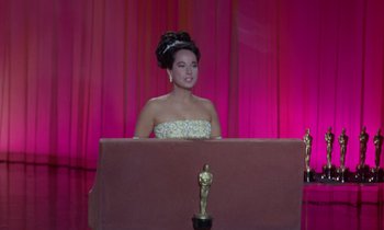 Movie still from “The Oscar” (1966), directed by Russell Rouse – A woman in a strapless dress sitting in front of an oscar statue; Wide shot, High angle