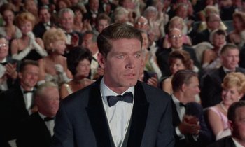 Movie still from “The Oscar” (1966), directed by Russell Rouse – A man standing in front of a crowd wearing a tuxedo; Medium shot, Over the shoulder angle