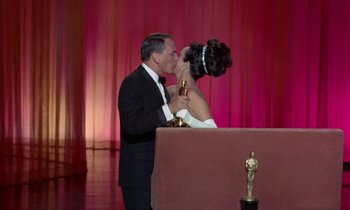 Movie still from “The Oscar” (1966), directed by Russell Rouse – A man and a woman kissing in front of an oscar statue; Wide shot, Low angle