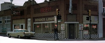 Movie still from “The Outsiders” (1983), directed by Francis Ford Coppola – A man standing in front of a brown building; Wide shot, High angle