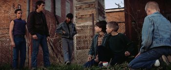Movie still from “The Outsiders” (1983), directed by Francis Ford Coppola – Three young boys sitting on the ground in a yard; Wide shot, Over the shoulder angle
