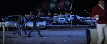 Movie still from “The Outsiders” (1983), directed by Francis Ford Coppola – A man walking across a parking lot at night; Wide shot, Over the shoulder angle