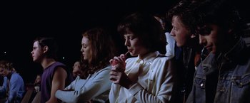 Movie still from “The Outsiders” (1983), directed by Francis Ford Coppola – A group of people sitting next to each other holding drinks; Medium shot, High angle