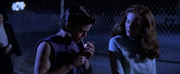 Movie still from “The Outsiders” (1983), directed by Francis Ford Coppola – A woman smoking a cigarette next to another woman; Medium shot, Over the shoulder angle