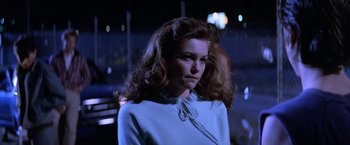 Movie still from “The Outsiders” (1983), directed by Francis Ford Coppola – A woman with long red hair standing in front of a building; Close Up shot, Over the shoulder angle