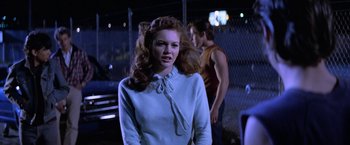 Movie still from “The Outsiders” (1983), directed by Francis Ford Coppola – A young woman standing in front of two other people; Medium shot, Over the shoulder angle