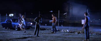 Movie still from “The Outsiders” (1983), directed by Francis Ford Coppola – Two men standing next to each other on a dirt field at night; Wide shot, Low angle