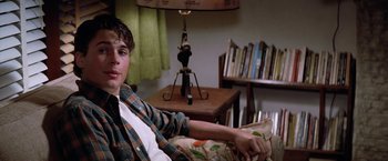 Movie still from “The Outsiders” (1983), directed by Francis Ford Coppola – A man sitting on top of a couch in a living room; Medium shot, Over the shoulder angle