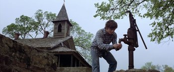 Movie still from “The Outsiders” (1983), directed by Francis Ford Coppola – A man holding a hammer in front of an old church; Medium shot, Low angle