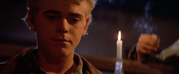 Movie still from “The Outsiders” (1983), directed by Francis Ford Coppola – A young man with blonde hair stares at a candle; Close Up shot, Over the shoulder angle