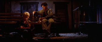Movie still from “The Outsiders” (1983), directed by Francis Ford Coppola – A man sitting on top of a bench holding a candle; Medium shot, Low angle