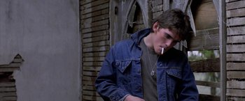 Movie still from “The Outsiders” (1983), directed by Francis Ford Coppola – A young man smoking a cigarette while wearing a jean jacket; Close Up shot, Over the shoulder angle