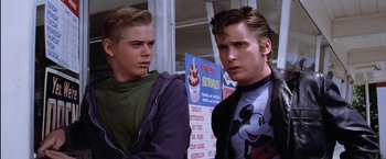 Movie still from “The Outsiders” (1983), directed by Francis Ford Coppola – Two young men standing next to each other in front of signs; Close Up shot, Over the shoulder angle
