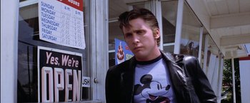 Movie still from “The Outsiders” (1983), directed by Francis Ford Coppola – A man in a mickey mouse shirt standing in front of a store window; Medium shot, Low angle