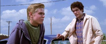 Movie still from “The Outsiders” (1983), directed by Francis Ford Coppola – Two young men standing next to each other near a parked car; Close Up shot, Low angle