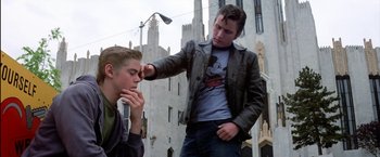 Movie still from “The Outsiders” (1983), directed by Francis Ford Coppola – Two young men standing in front of tall buildings; Medium shot, Low angle
