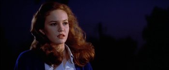 Movie still from “The Outsiders” (1983), directed by Francis Ford Coppola – A woman with long red hair is standing in a dark room; Close Up shot, Low angle