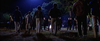 Movie still from “The Outsiders” (1983), directed by Francis Ford Coppola – A group of people standing around a campfire at night; Wide shot, High angle