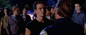 Movie still from “The Outsiders” (1983), directed by Francis Ford Coppola – A man that is standing in front of a group of people; Close Up shot, Over the shoulder angle