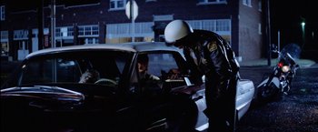 Movie still from “The Outsiders” (1983), directed by Francis Ford Coppola – A police officer checking the id of a person in a car; Medium shot, Over the shoulder angle