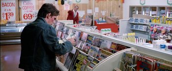 Movie still from “The Outsiders” (1983), directed by Francis Ford Coppola – A woman looking at magazines in a store; Medium shot, Over the shoulder angle